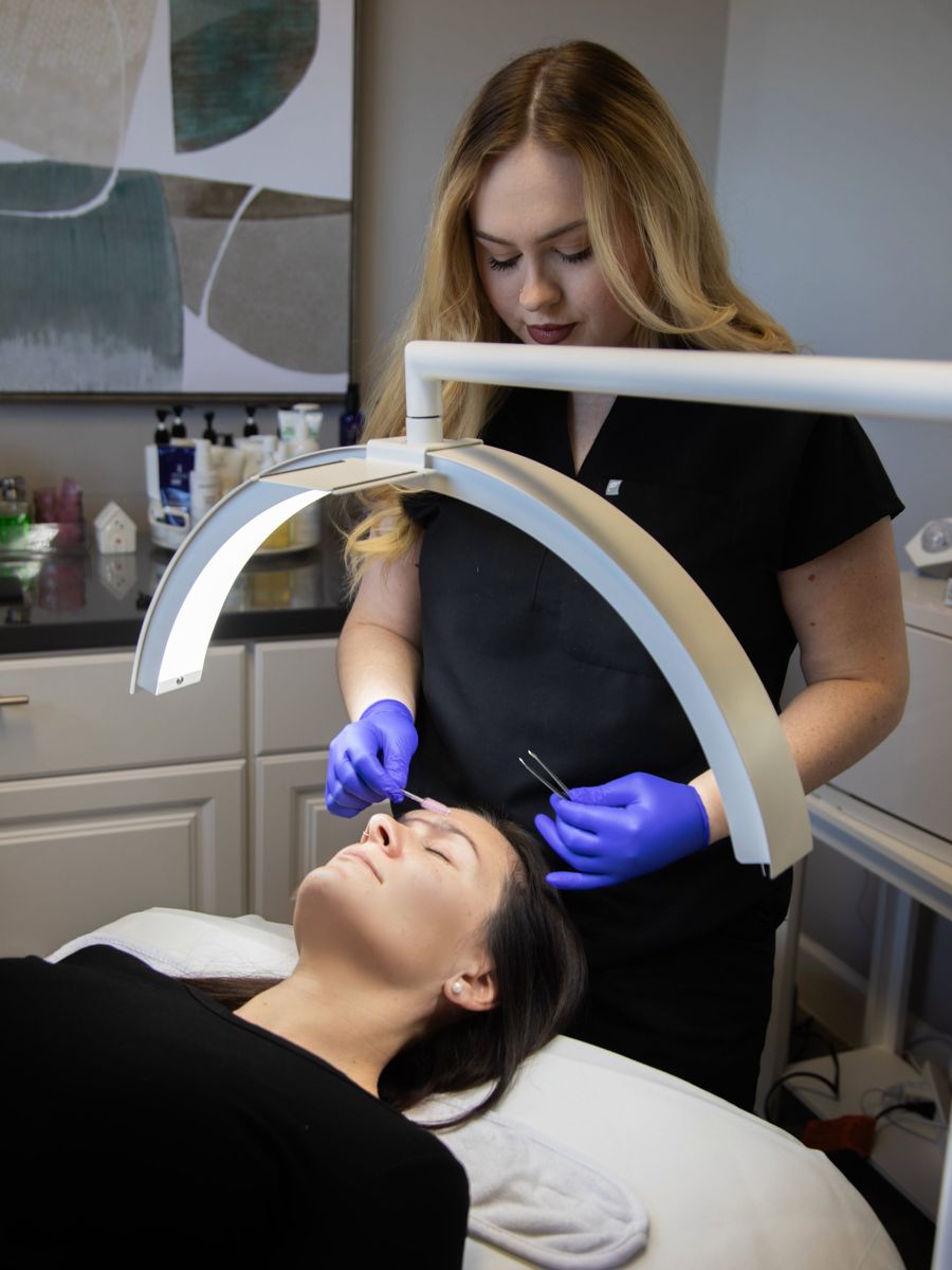 Esthetician examining a client's skin under a magnifying lamp